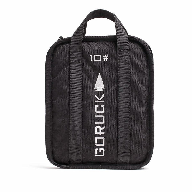 A rugged-textured Rucker bag in black from GORUCK, featuring two handles and adorned with GORUCK and 10 printed in white alongside an arrow design. The front showcases vertical stitching lines, and it comes with a lifetime guarantee for ultimate peace of mind.
