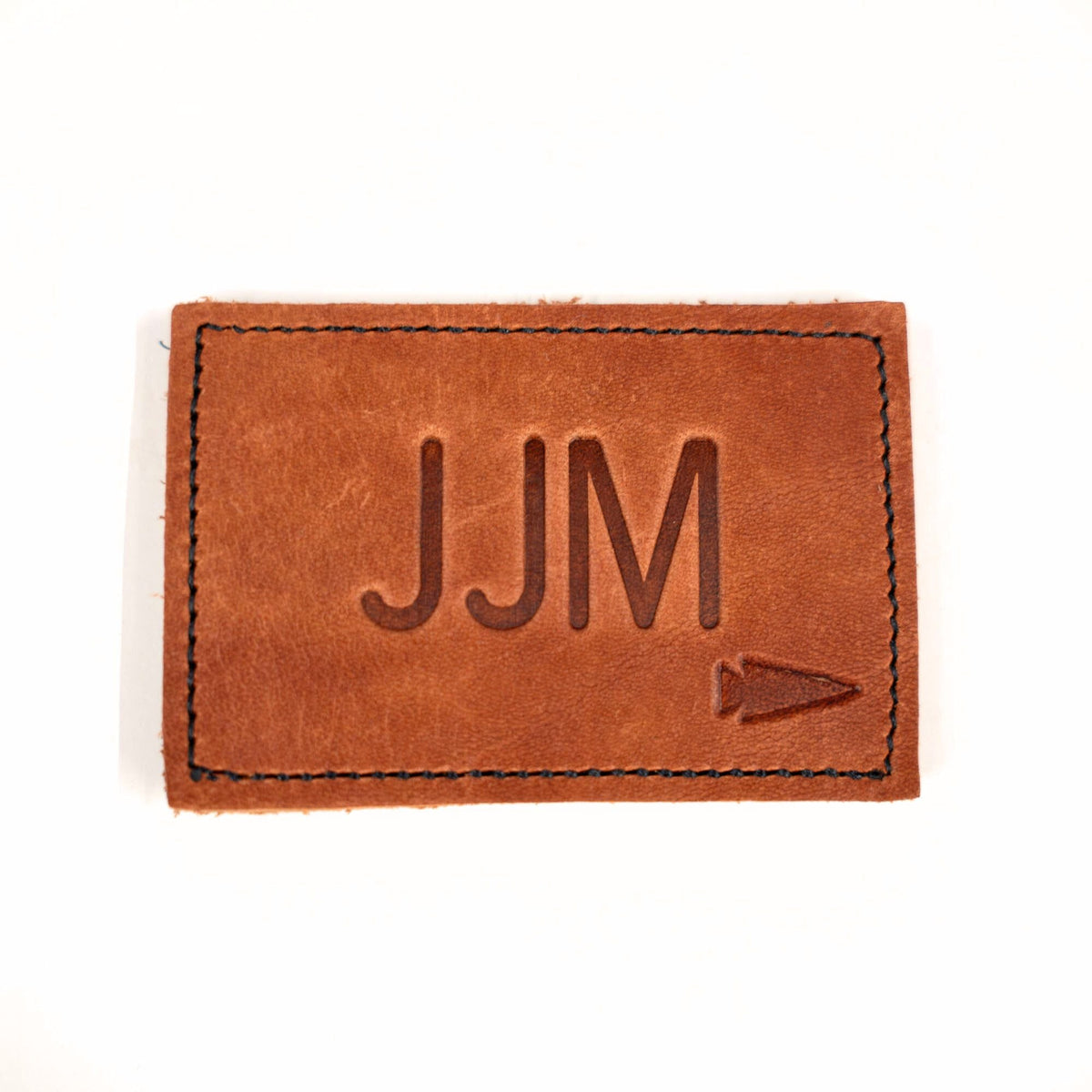 Patch - Custom Leather Monogram: brown leather patch embossed with custom initials "JJM" and an arrow symbol—perfect for adding a unique, personalized touch.