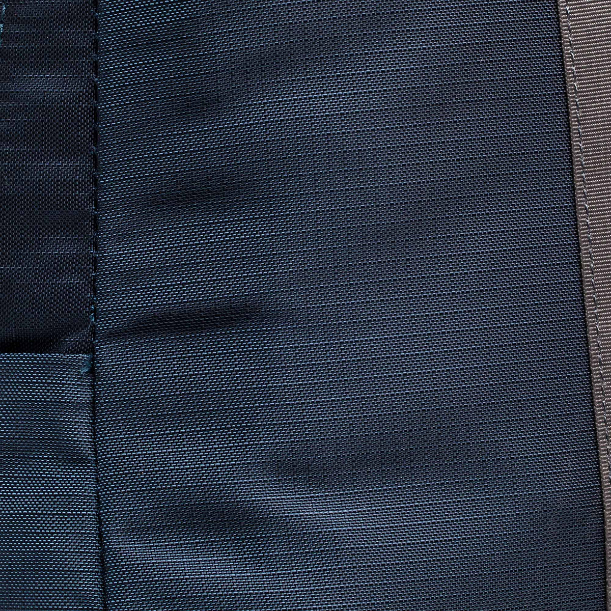 Close-up of dark blue fabric with a vertical seam and visible stitching details, similar to the rugged materials used in the Basic Rucker.