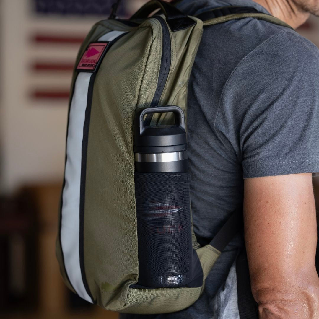 A person wearing a green Basic Rucker with a water bottle in the side pocket, American flag in the background.