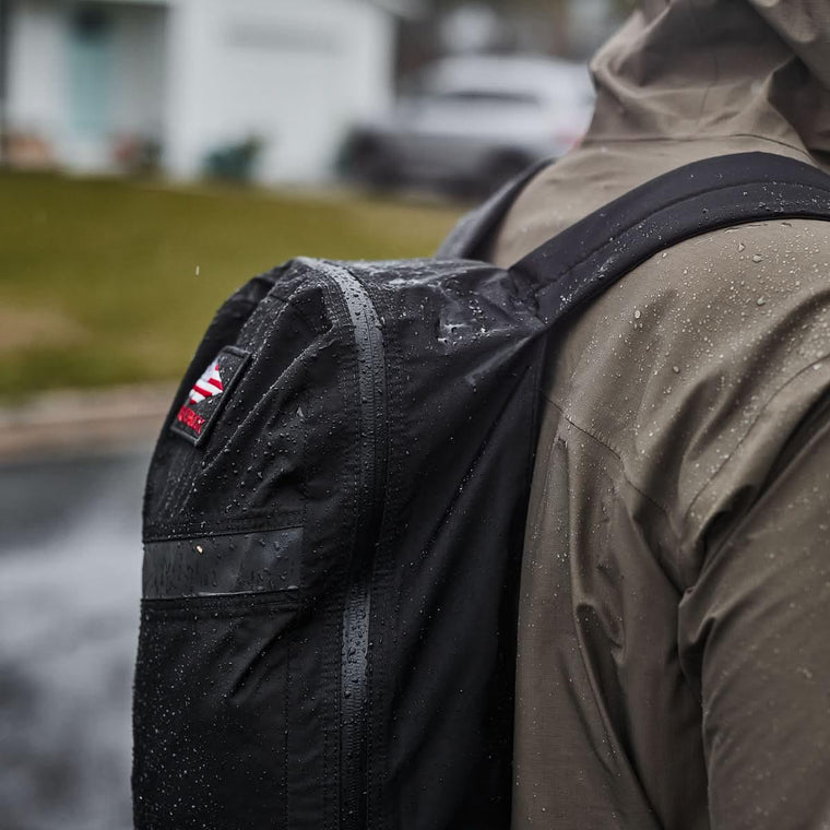 A person wearing a rain jacket and a lightweight day bag with AquaGuard zippers in the rain.