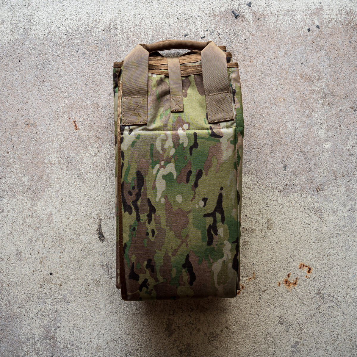 A folded camouflage-patterned Shooting Mat rests on a textured concrete surface.