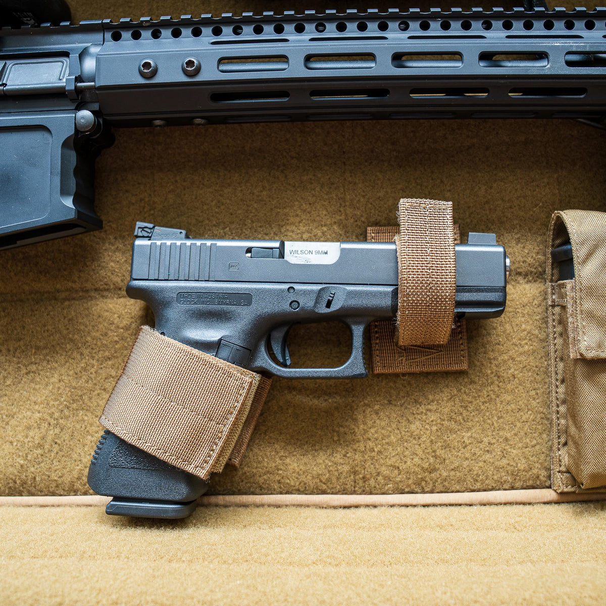 A Retention Package featuring a black handgun secured with brown straps inside a tan padded case, shown below part of a rifle.