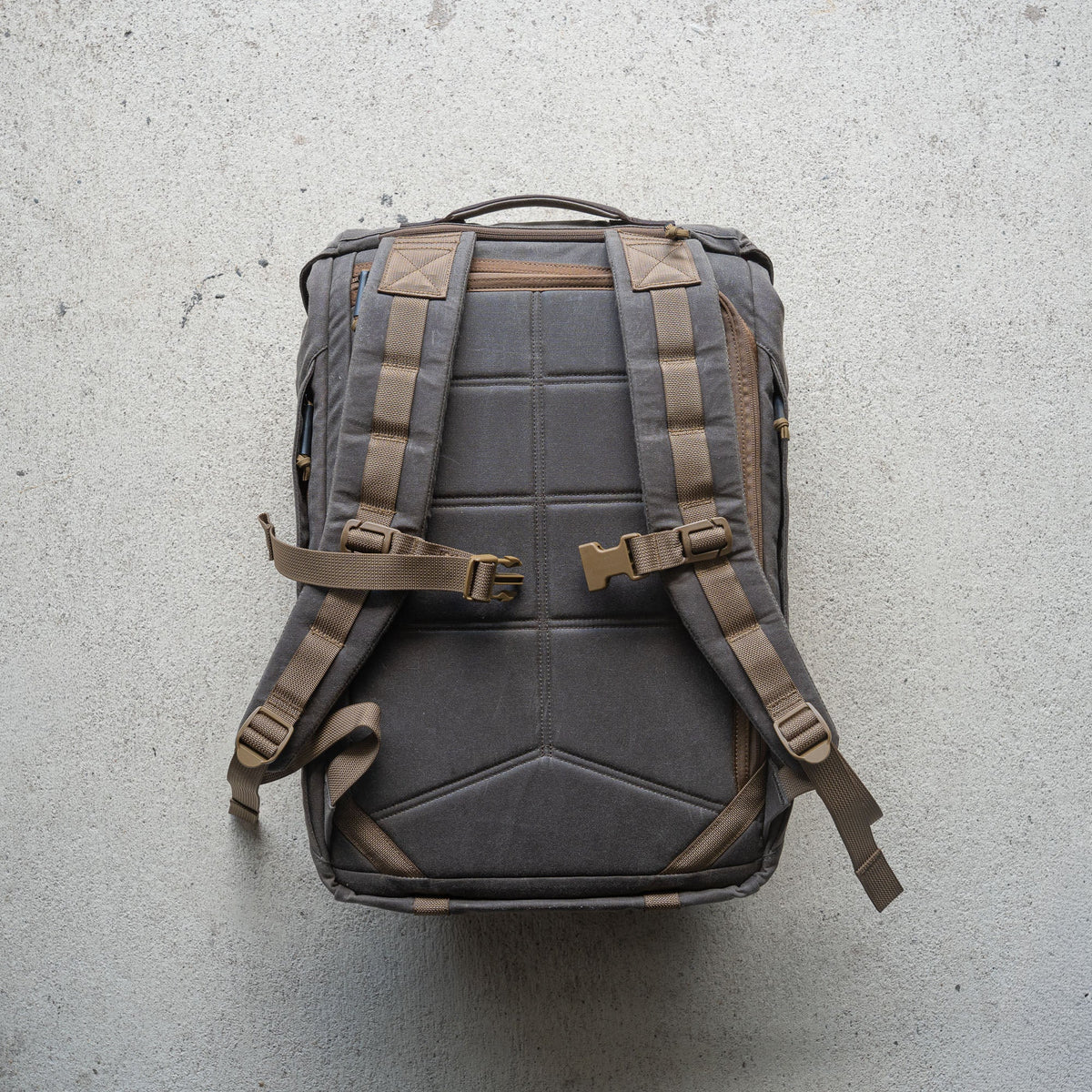 The M26 PREORDER // Q4 2026 ETA backpack, featuring padded straps, buckles, and a bombproof laptop compartment, is displayed flat on a textured light-colored surface.