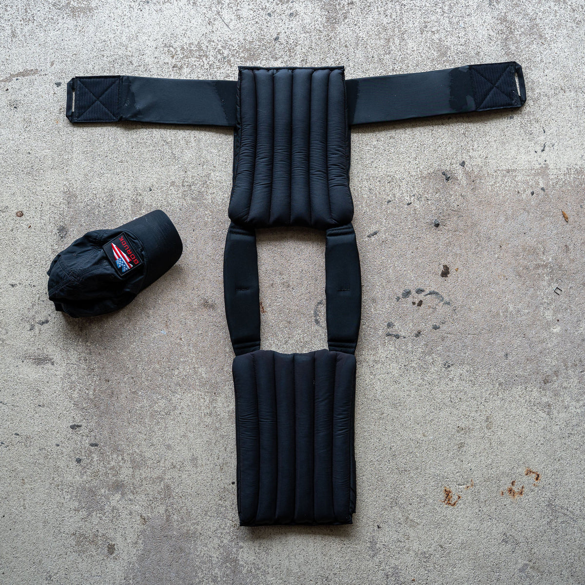 The Achilles | Men's Weighted Vest, featuring padded non-toxic construction, is laid flat on concrete beside a black baseball cap.