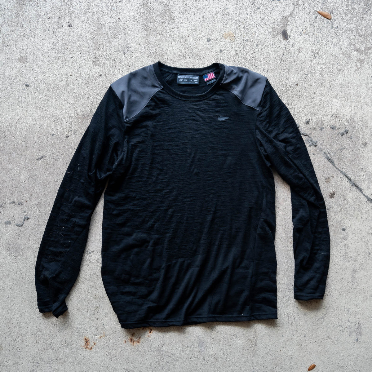 Men’s Commando Long Sleeve - Merino Wool in black, featuring reinforced shoulders and a classic commando sweater design, laid flat on a concrete surface.