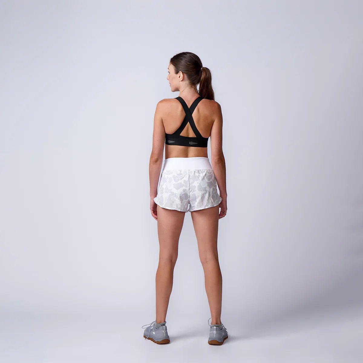 Woman wearing GORUCK sports bra and camo shorts, rucking gear studio shoot, rear view
