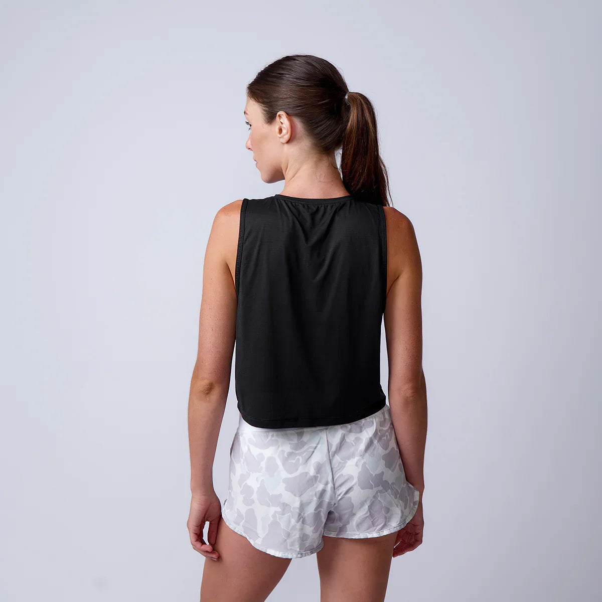 Woman wearing GORUCK black tank top and camo shorts, back view, against a plain background