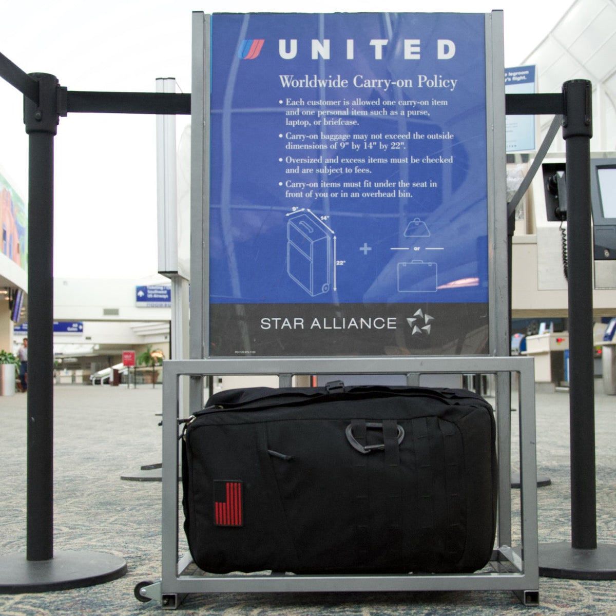 A GR2 USA - Cordura black travel backpack under a United Airlines baggage size checker at an airport.