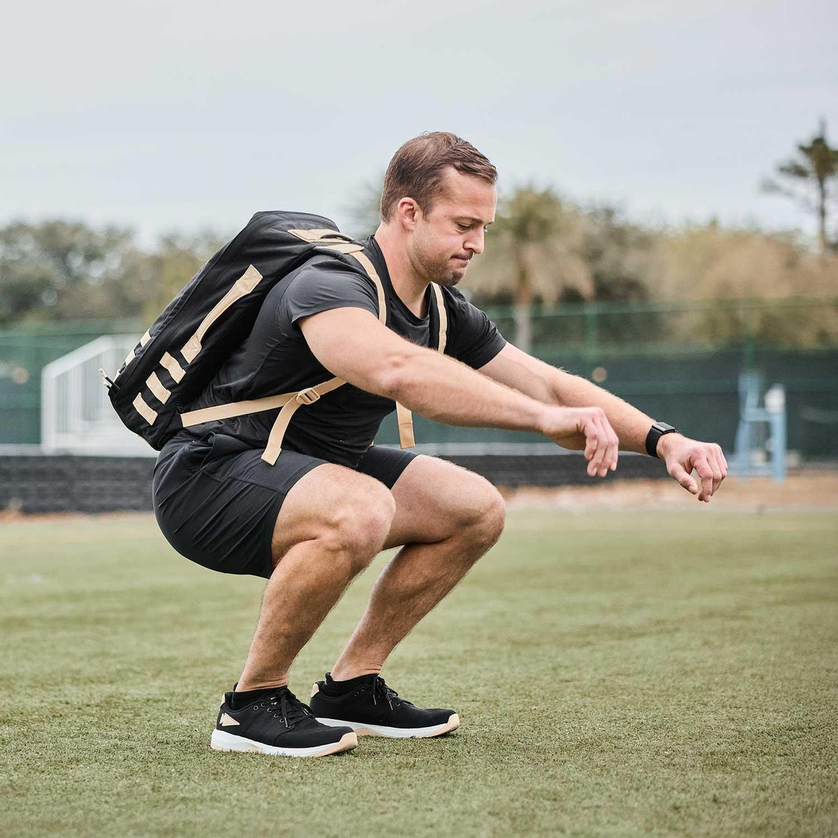 Man doing outdoor squat exercise wearing black GORUCK rucksack and athletic gear