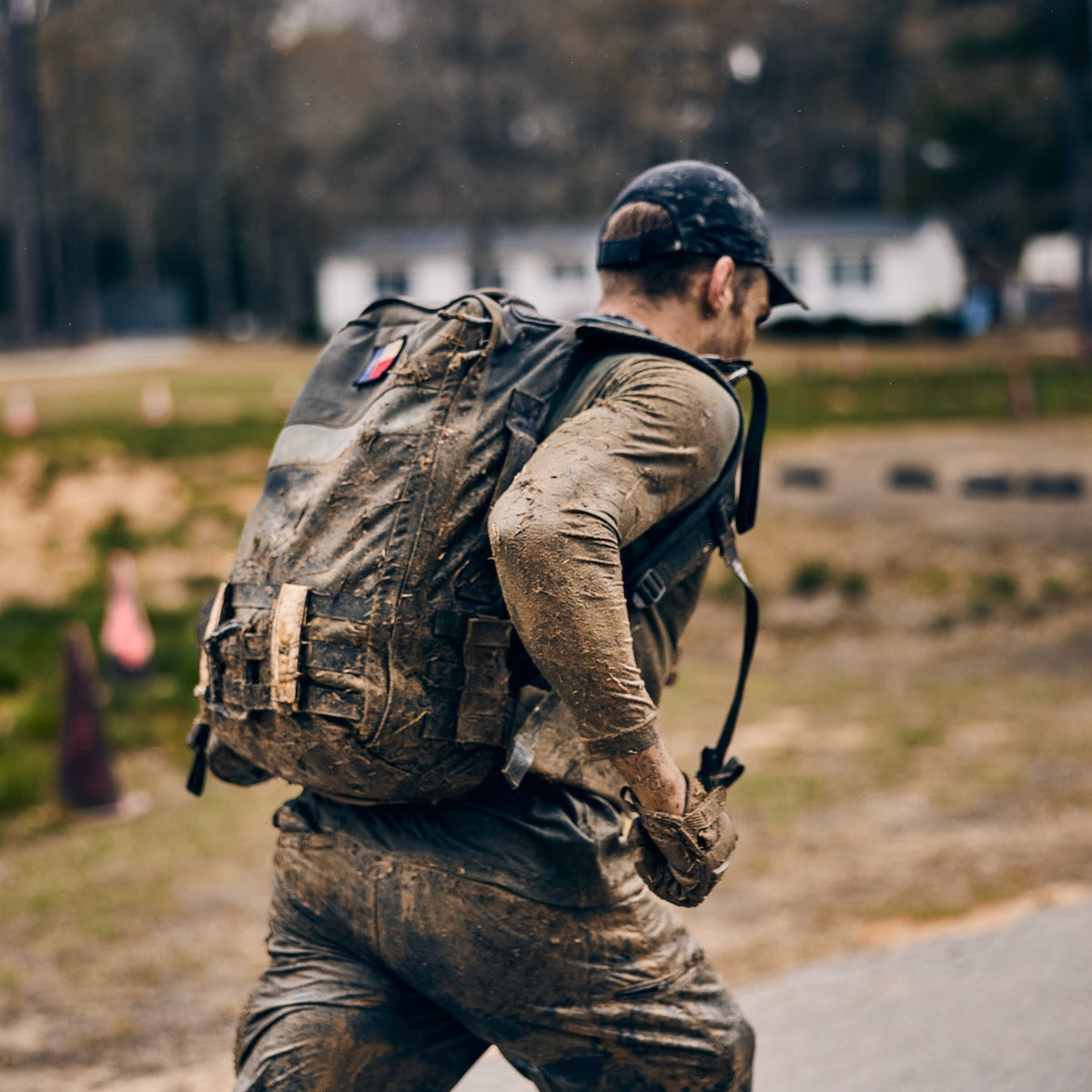 A person covered in mud carrying a muddy backpack runs along a path wearing abrasion-resistant, fast-drying pants.