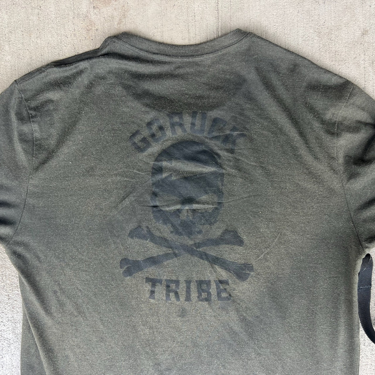 Olive green GORUCK Tribe t-shirt with a black skull and crossbones logo on the back.