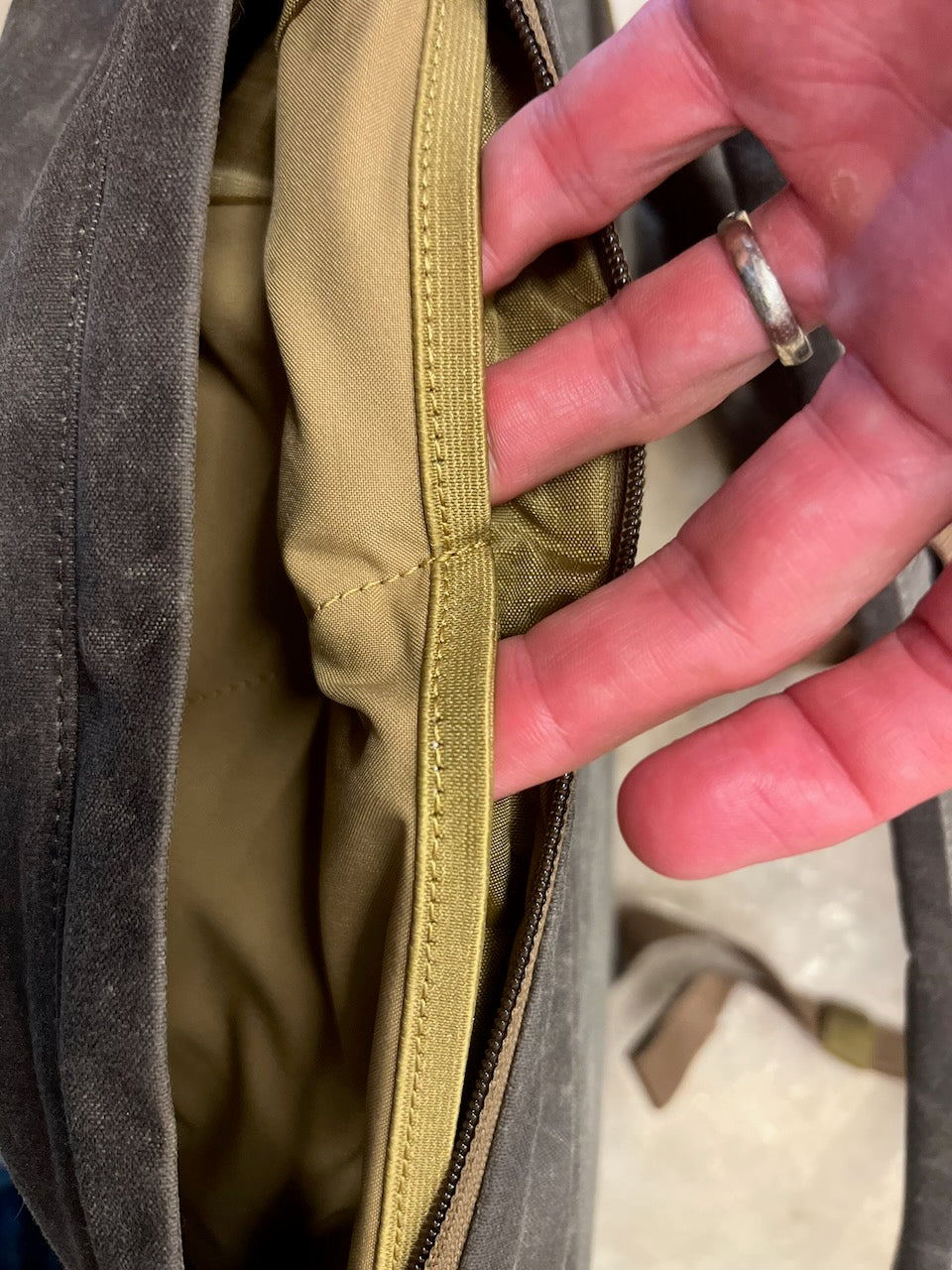 A hand pulls open the elasticized bombproof laptop compartment inside a gray WWII-inspired backpack.