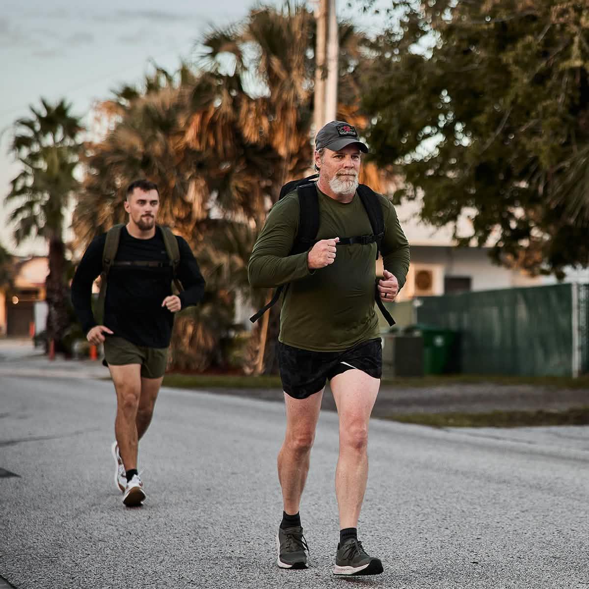 Two men rucking with GORUCK backpacks on a street, wearing athletic outdoor gear