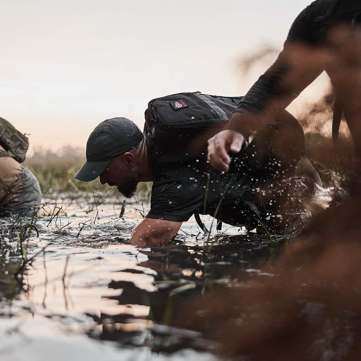 Man wearing GORUCK rucksack crawling through water during outdoor rucking challenge