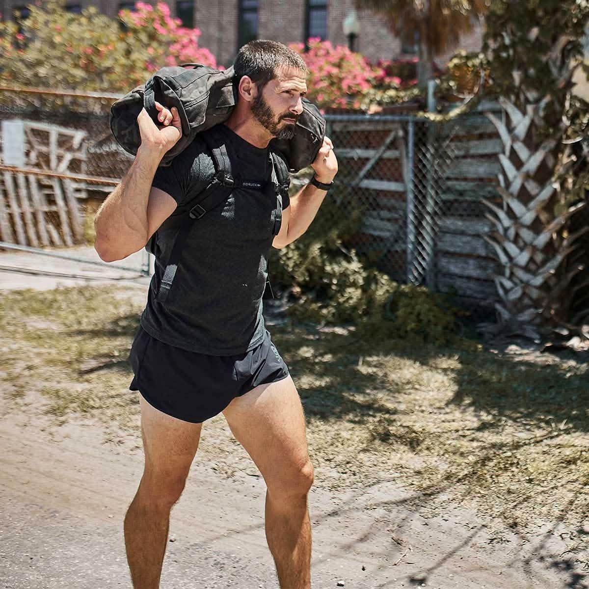 Man rucking outdoors with GORUCK gear, carrying weighted sandbag over shoulders