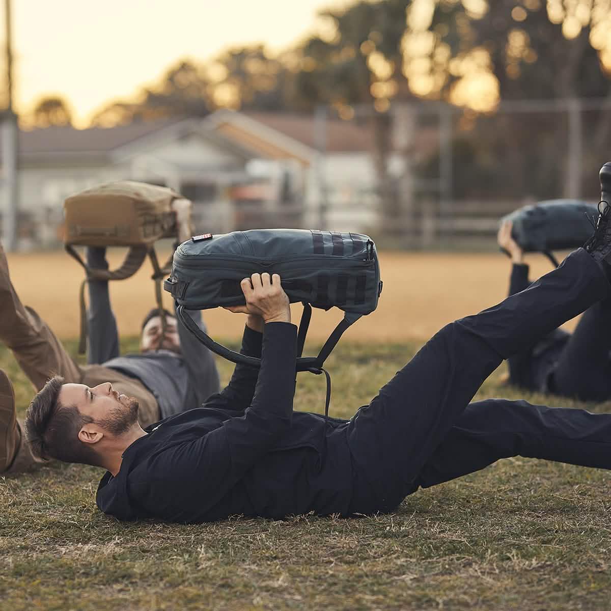 Men in outdoor fitness training using GORUCK rucksacks on grass at sunset